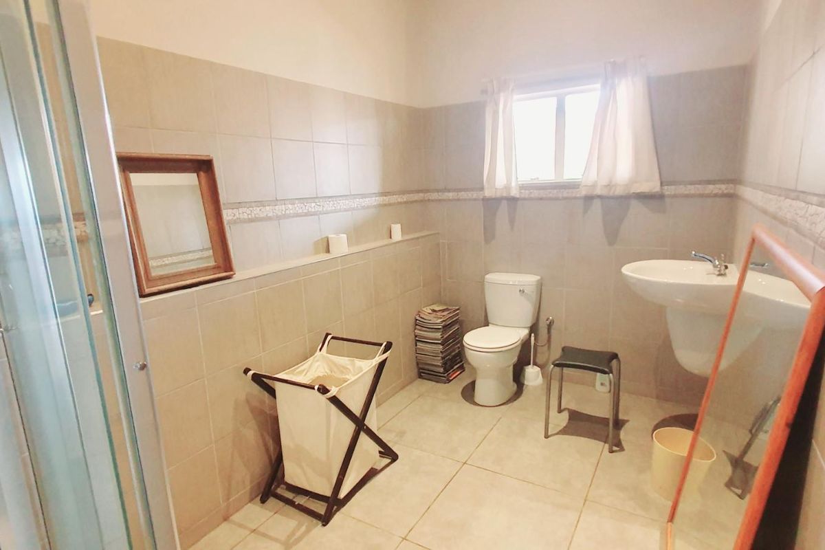 A functional bathroom featuring a shower enclosure, pedestal washbasin, and toilet, finished with neutral ceramic wall and floor tiles.