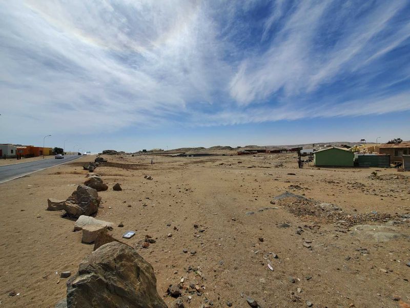 A wide-angle view of an undeveloped commercial plot of land adjacent to a paved road in a desert environment.
