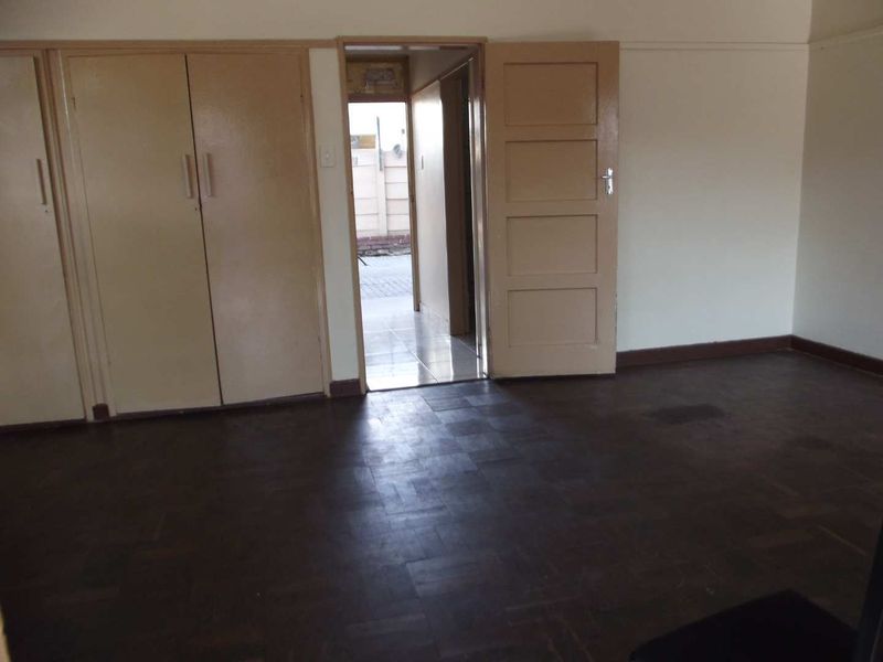 An empty bedroom featuring original parquet flooring and built-in cupboards, with a doorway leading to an exterior passage.