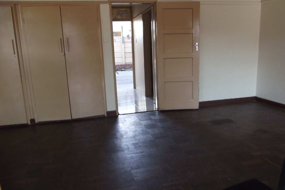 An empty bedroom featuring original parquet flooring and built-in cupboards, with a doorway leading to an exterior passage.