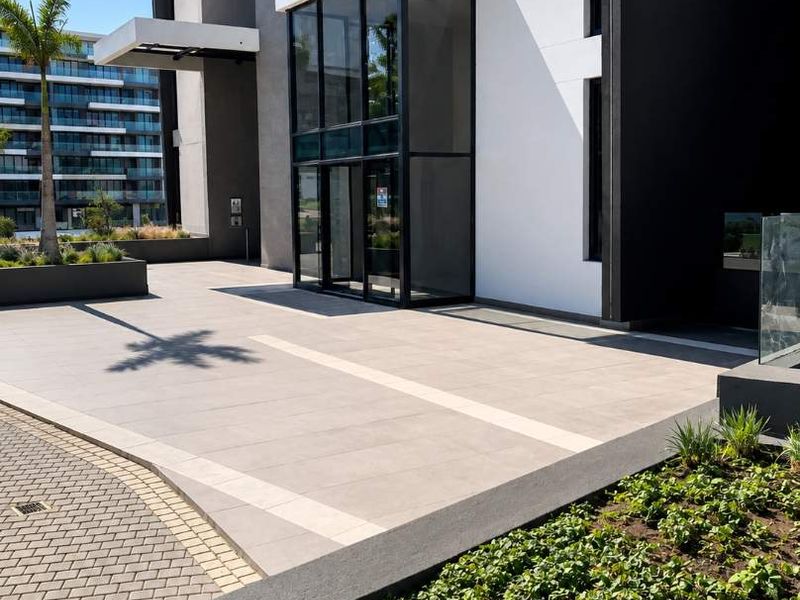 Modern retail building entrance featuring a glass facade, paved forecourt, and contemporary concrete planter boxes.