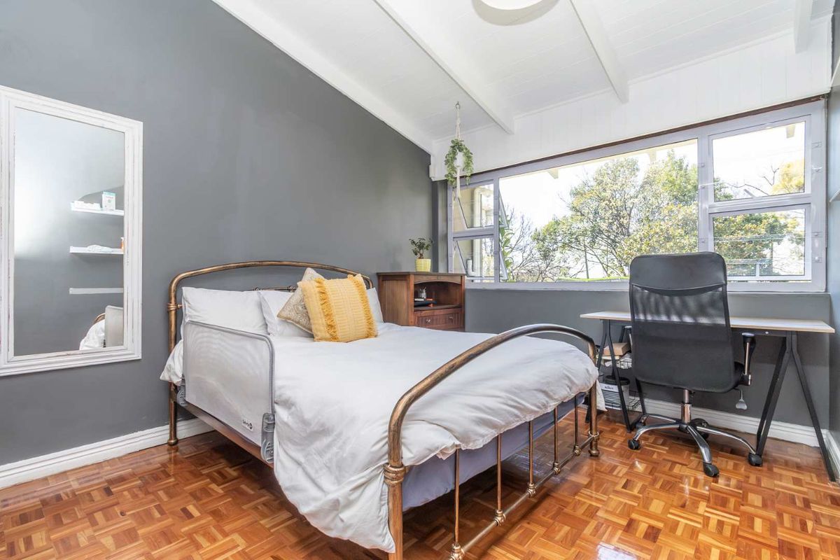 A well-lit bedroom featuring classic parquet flooring, a high exposed beam ceiling, and a large window providing natural light.