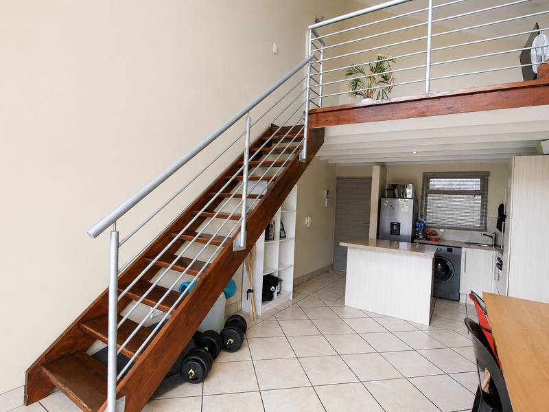 Open plan living area featuring a wooden staircase leading to a mezzanine level, tiled flooring, and a functional kitchen with an island.