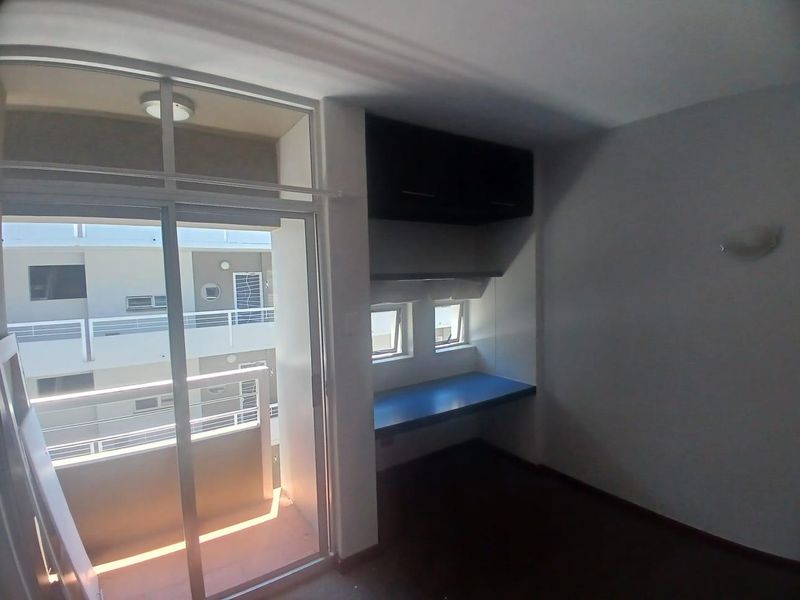 A bedroom featuring a built-in desk with overhead cabinetry and a sliding glass door providing access to a private balcony.