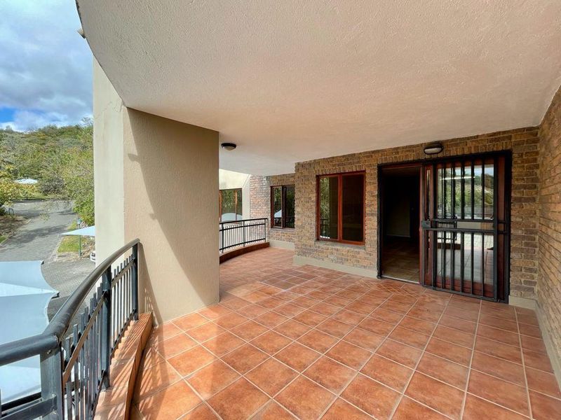 A spacious covered balcony featuring terracotta-style floor tiles, brick wall accents, and a secure metal gate entrance, offering an open outdoor living space.