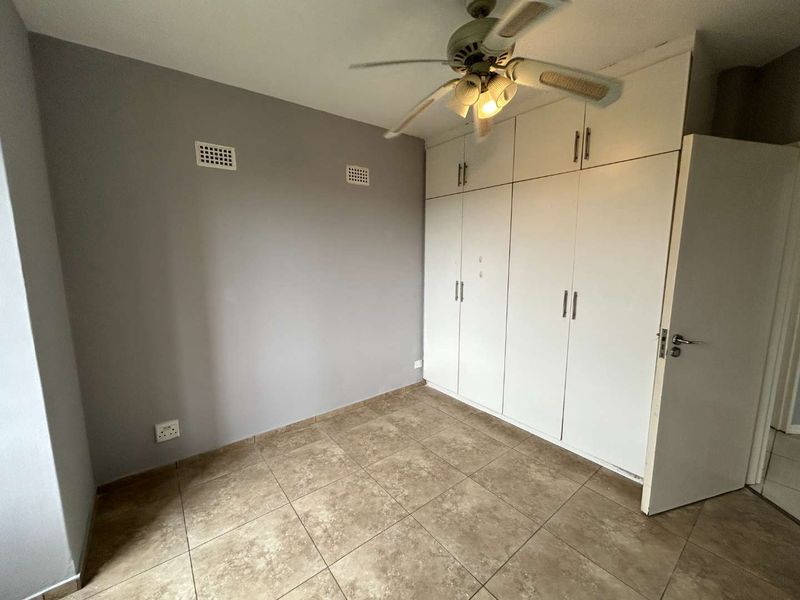 A vacant bedroom featuring tiled flooring, built-in cupboards with overhead storage, and a ceiling fan.