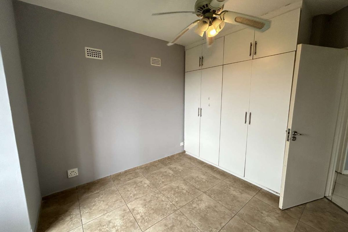 A vacant bedroom featuring tiled flooring, built-in cupboards with overhead storage, and a ceiling fan.
