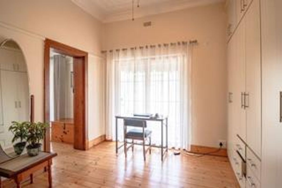 A bright bedroom featuring polished timber flooring, built-in cupboards, and classic architectural details including a ceiling rose and timber door frames.