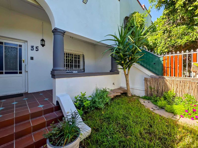 Front entrance of the townhouse featuring a tiled porch, decorative columns, and a small garden area with security features.