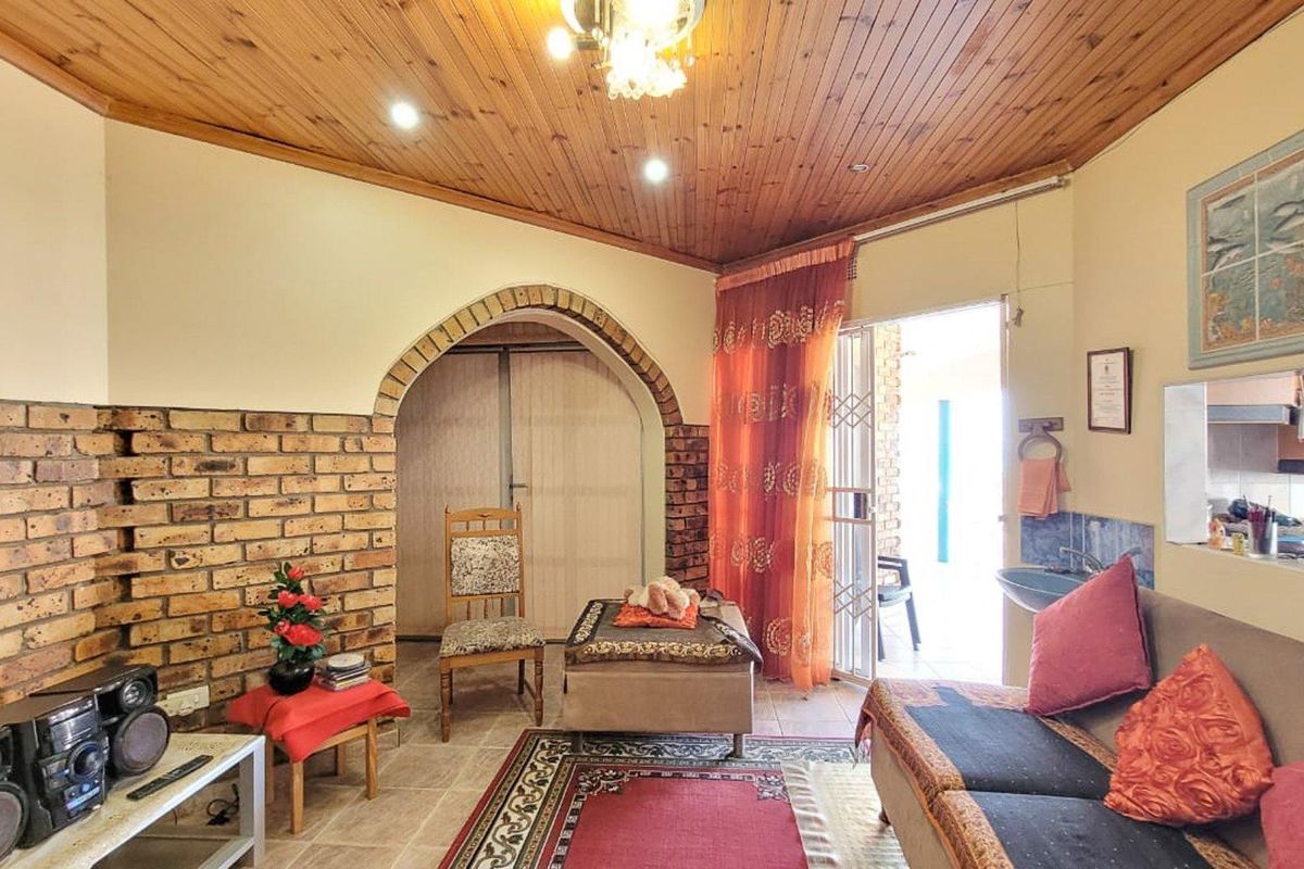 A living room featuring a distinctive brick archway, exposed brick feature wall, and timber-clad vaulted ceiling with access to an outdoor patio area.