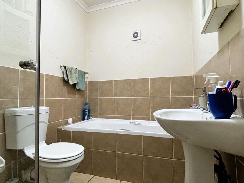 A functional bathroom featuring a pedestal basin, toilet, and a built-in bathtub with shower enclosure, finished with neutral wall tiling.