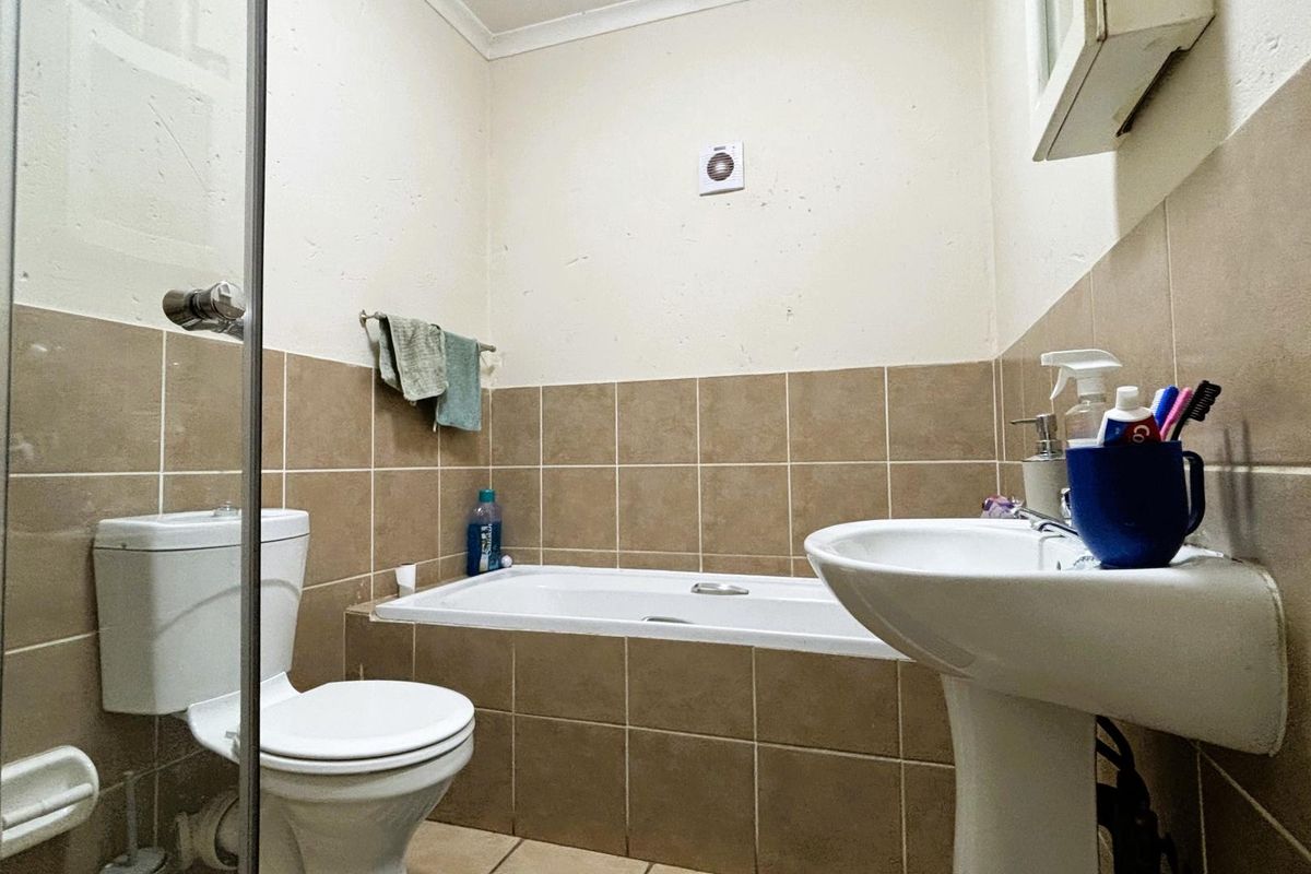 A functional bathroom featuring a pedestal basin, toilet, and a built-in bathtub with shower enclosure, finished with neutral wall tiling.