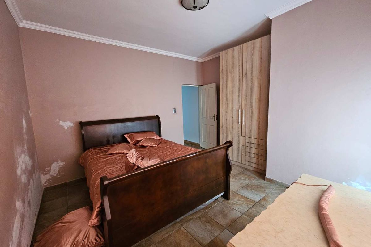 A bedroom featuring tiled flooring, a built-in wardrobe, and visible wall damage requiring repair and repainting.