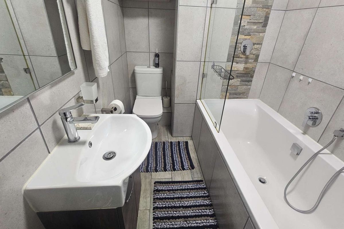 Modern bathroom featuring a vanity basin, toilet, and a bathtub with a glass shower screen and stone feature wall detailing.
