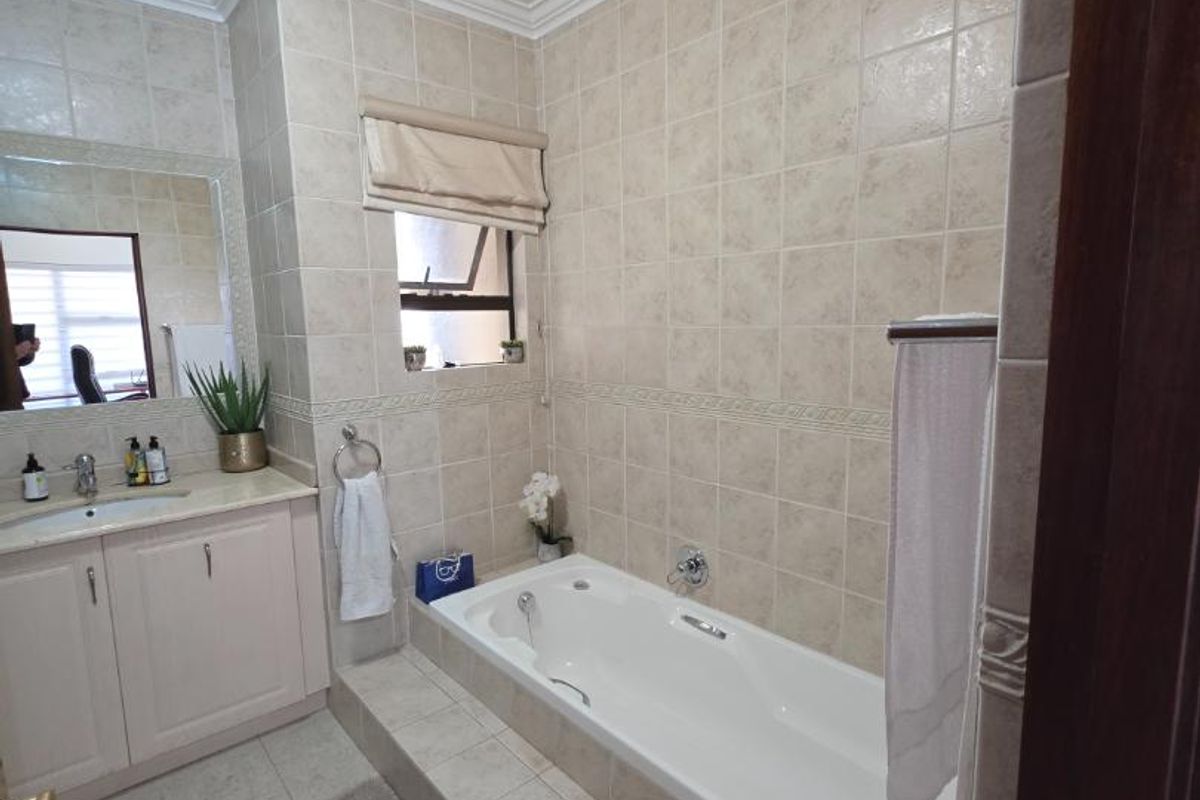 A well-maintained bathroom featuring a built-in vanity with basin, a tiled drop-in bathtub, and neutral wall tiling with decorative border accents.
