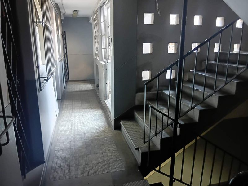A communal apartment hallway featuring a staircase with metal balustrades, tiled flooring, and decorative ventilation blocks.