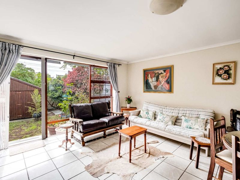 A bright living room featuring ceramic floor tiles and a large sliding glass door providing direct access to the rear garden area.
