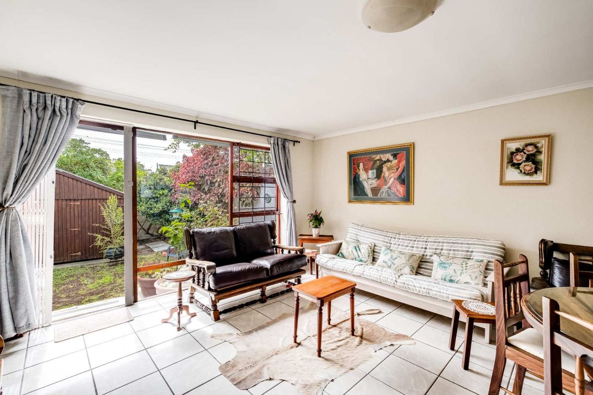 A bright living room featuring ceramic floor tiles and a large sliding glass door providing direct access to the rear garden area.