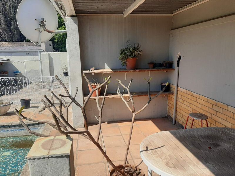 A covered outdoor patio area featuring tiled flooring, brick wall accents, and built-in shelving, overlooking the pool area.