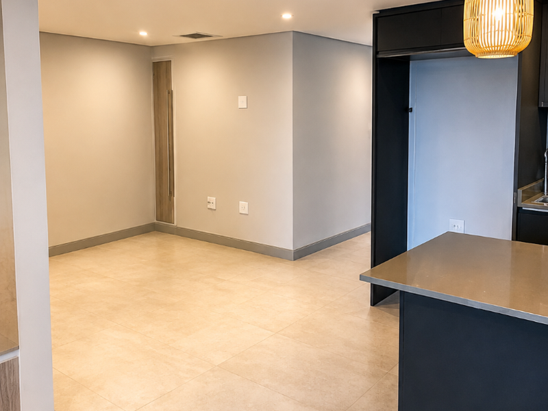 A modern, open-plan living and kitchen area featuring neutral tiled flooring, recessed lighting, and a sleek kitchen island with a stainless steel countertop.