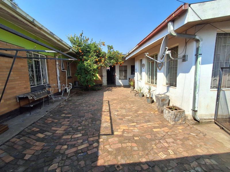 A rear courtyard area featuring brick paving, established citrus tree, and access to the main dwelling structure.