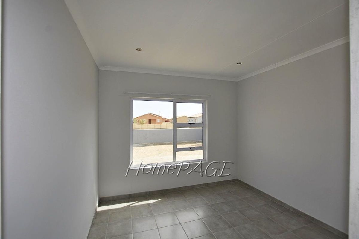 A bright, empty bedroom featuring neutral tiled flooring, recessed ceiling lighting, and a large window providing natural light.