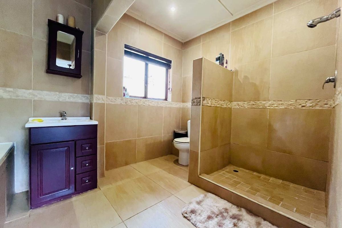 A functional bathroom featuring a walk-in shower with a half-wall partition, a vanity cabinet with basin, and neutral floor-to-ceiling wall tiling.
