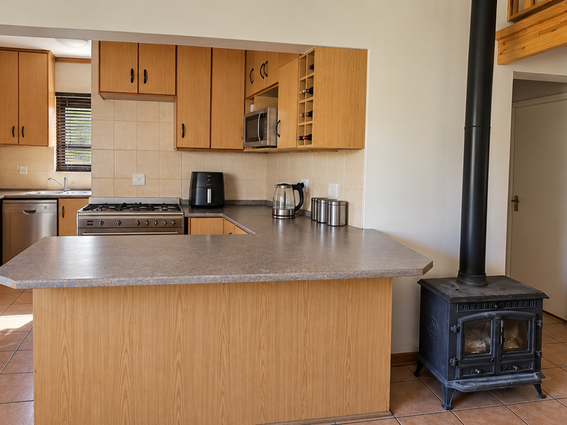 Open-plan kitchen featuring laminate cabinetry, gas stove, and breakfast bar, adjacent to a living area with a wood-burning fireplace and timber staircase.