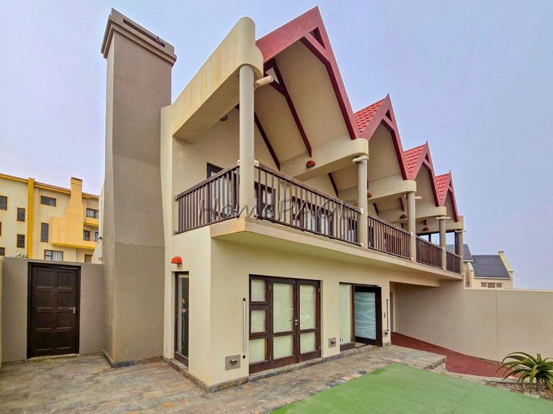Rear view of a multi-story residential property featuring a chimney, upper-level balconies with railings, and a paved patio area.