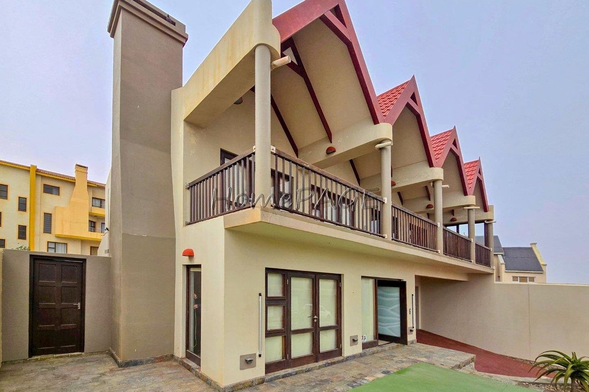 Rear view of a multi-story residential property featuring a chimney, upper-level balconies with railings, and a paved patio area.