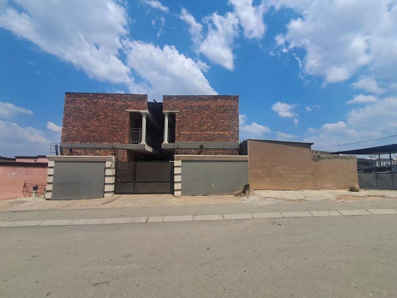 Front elevation of a face brick house featuring a perimeter wall, metal gate, and balcony with decorative columns.