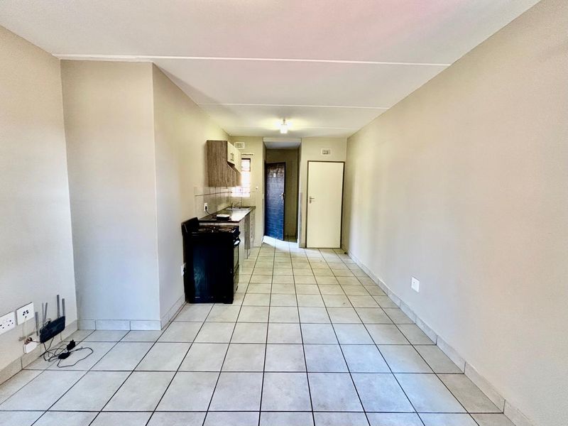 An open-plan living and kitchen area featuring tiled flooring, basic cabinetry, and a freestanding stove, presenting a functional blank canvas for potential updates.