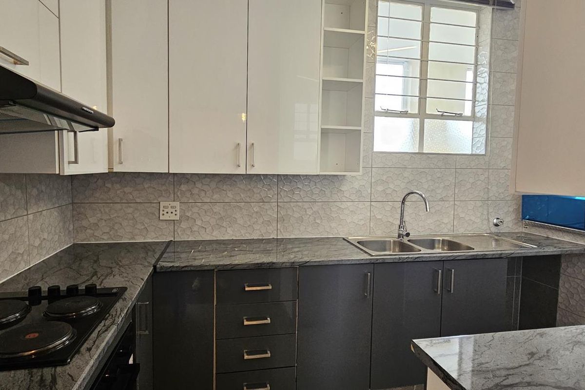 Modern kitchen featuring high-gloss cabinetry, granite countertops, a built-in electric hob with extractor fan, and a double bowl sink with tiled backsplash.