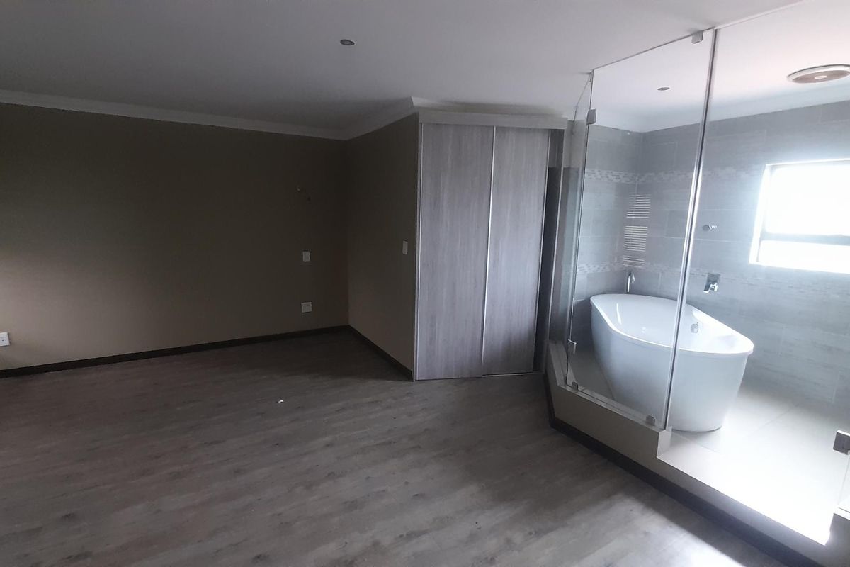 A spacious bedroom featuring modern laminate flooring, built-in cupboards, and an open-plan en-suite bathroom with a contemporary freestanding bathtub and glass enclosure.