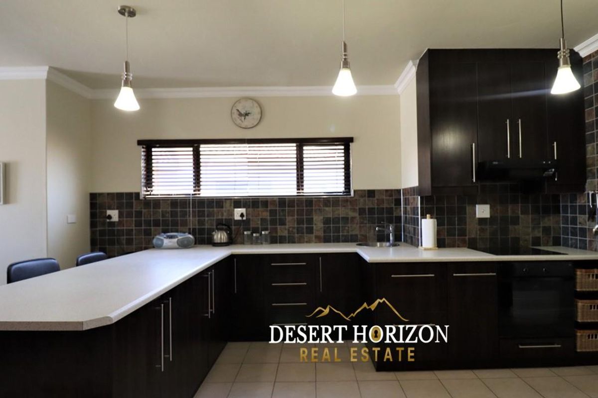 A functional kitchen featuring dark cabinetry, contrasting light countertops, tiled backsplash, and modern pendant lighting.