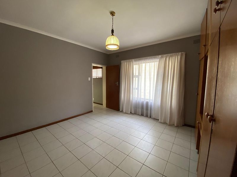 A spacious, empty bedroom featuring neutral grey walls, tiled flooring, and built-in wooden cupboards, offering a clean canvas for personalization.