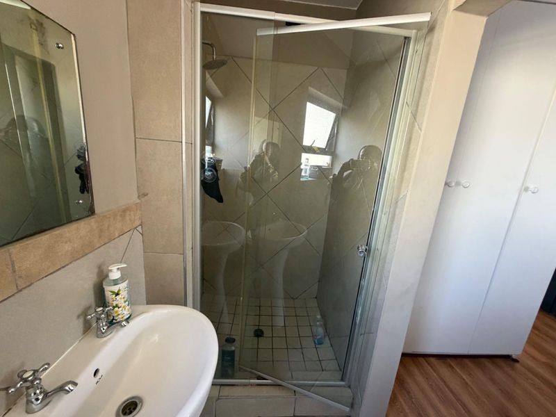 A functional bathroom featuring a pedestal basin, a glass-enclosed shower with tiled walls, and built-in storage cabinetry.