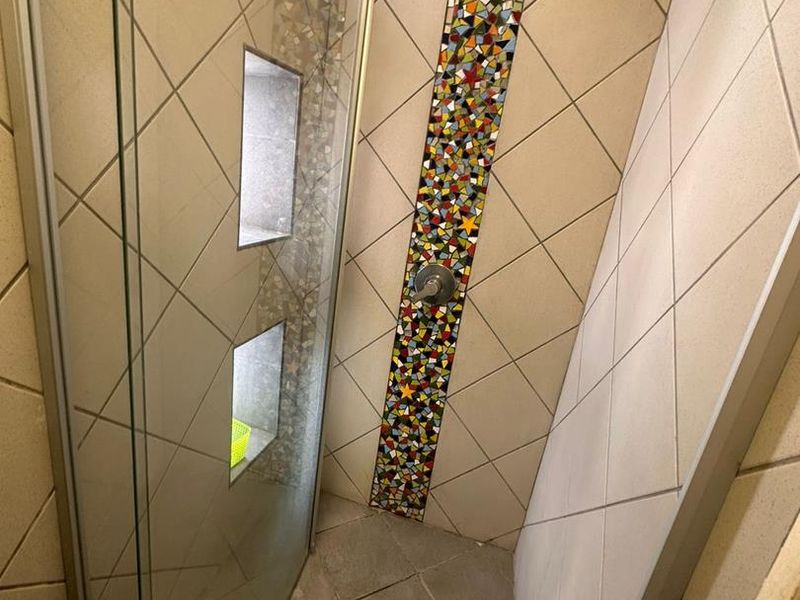 A walk-in shower featuring a mosaic tile accent strip, recessed wall niches, and a glass enclosure.