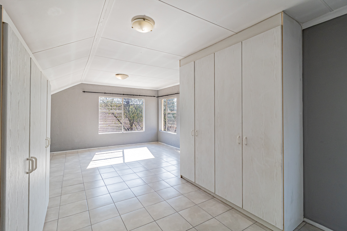 A spacious, empty bedroom featuring neutral tiled flooring, built-in cupboards, and large windows that provide ample natural light.