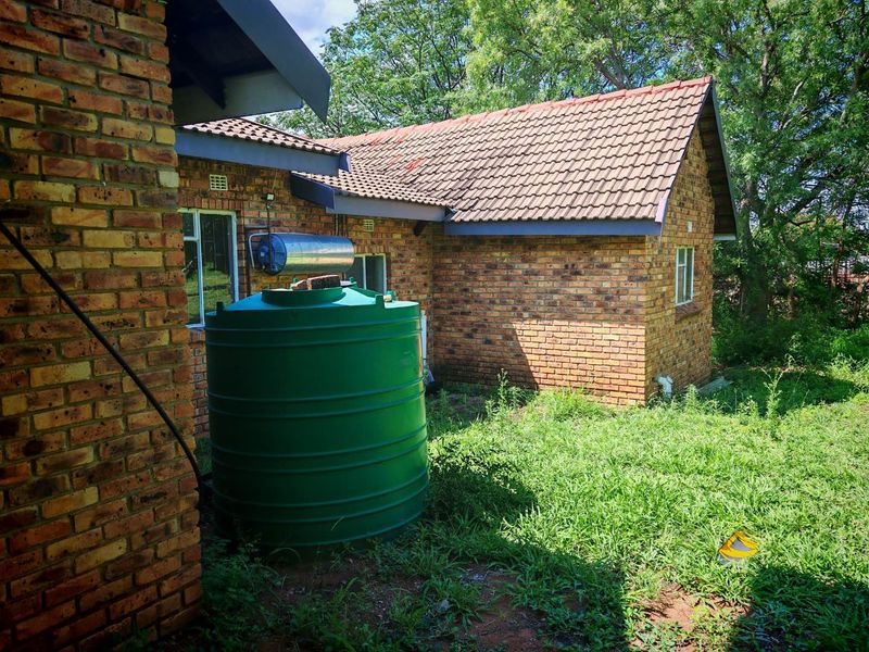 Rear exterior view of a face brick house featuring a water storage tank, solar geyser, and surrounding garden area.