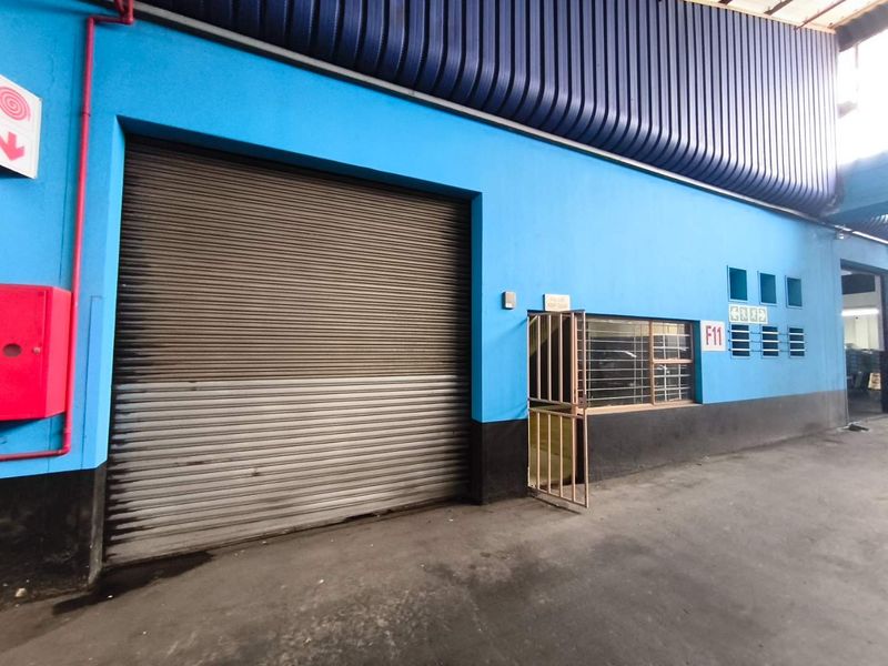 Industrial warehouse unit exterior featuring a large roller shutter door, security gate, and fire safety equipment.