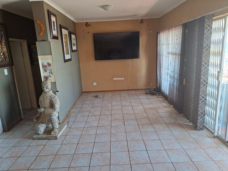 A spacious living area featuring ceramic tiled flooring, a wall-mounted television, and large sliding glass doors leading to an outdoor space.