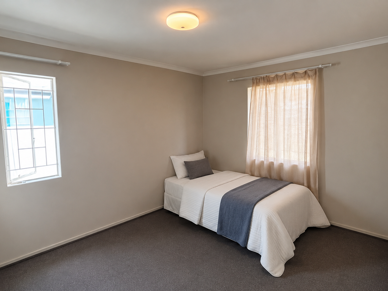 A clean and well-maintained bedroom featuring neutral wall tones, carpeted flooring, a built-in cupboard, and security bars on the window.