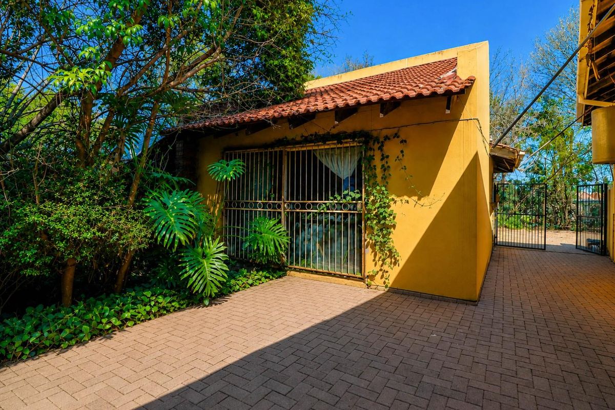 Rear exterior view of the property featuring a paved courtyard, terracotta roof tiles, and security-barred windows surrounded by established garden greenery.