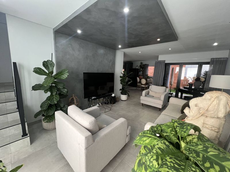 Modern open-plan living area featuring a striking dark textured ceiling feature, recessed lighting, large format floor tiles, and seamless access to the outdoor patio.
