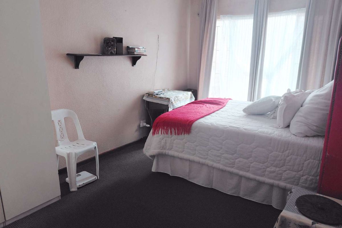 A standard bedroom featuring carpeted flooring, a built-in wardrobe, and large windows with curtain rails, providing natural light.