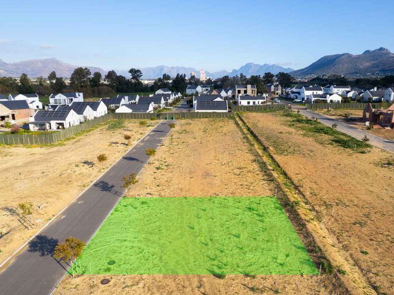 Aerial view of a vacant residential plot in a developed estate, featuring paved road access and surrounding mountain views.