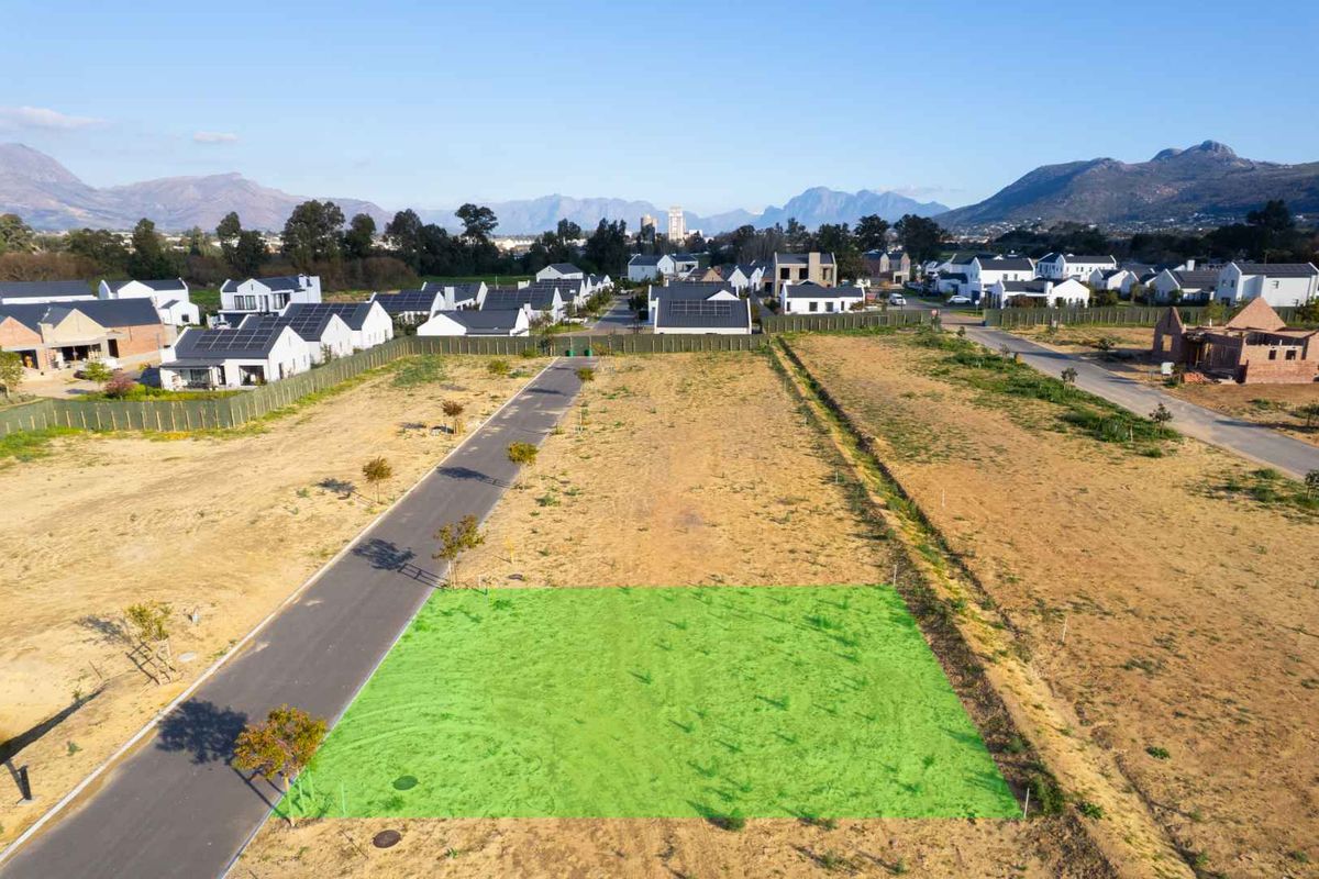 Aerial view of a vacant residential plot in a developed estate, featuring paved road access and surrounding mountain views.