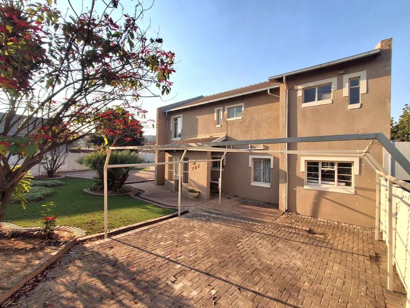 Front elevation of a two-story house featuring a paved driveway, carport structure, and established garden area.