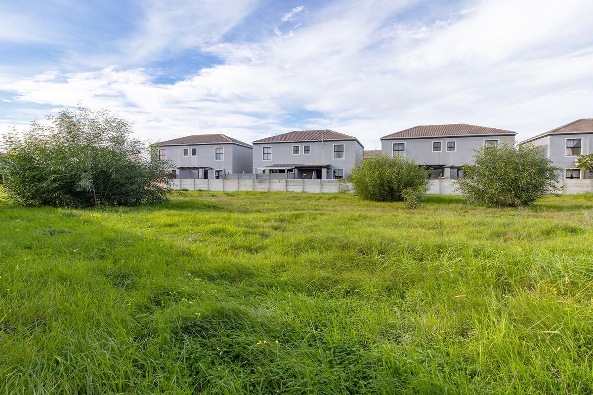 A vacant residential plot featuring natural grass cover and a precast concrete boundary wall, situated in a developed residential neighborhood.